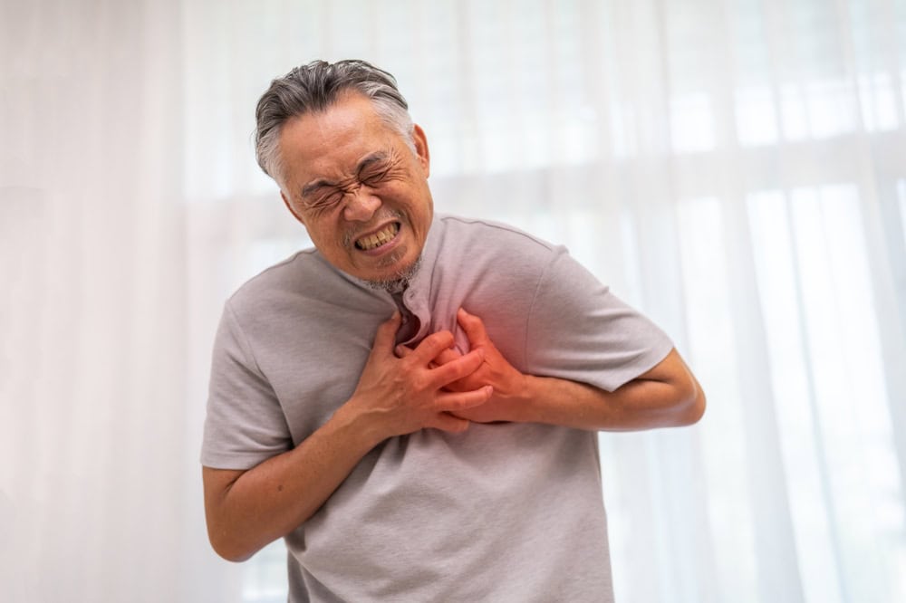 man holding his chest showing symptoms of a heart attack | Dr Gerard Leong Heart Specialist Singapore
