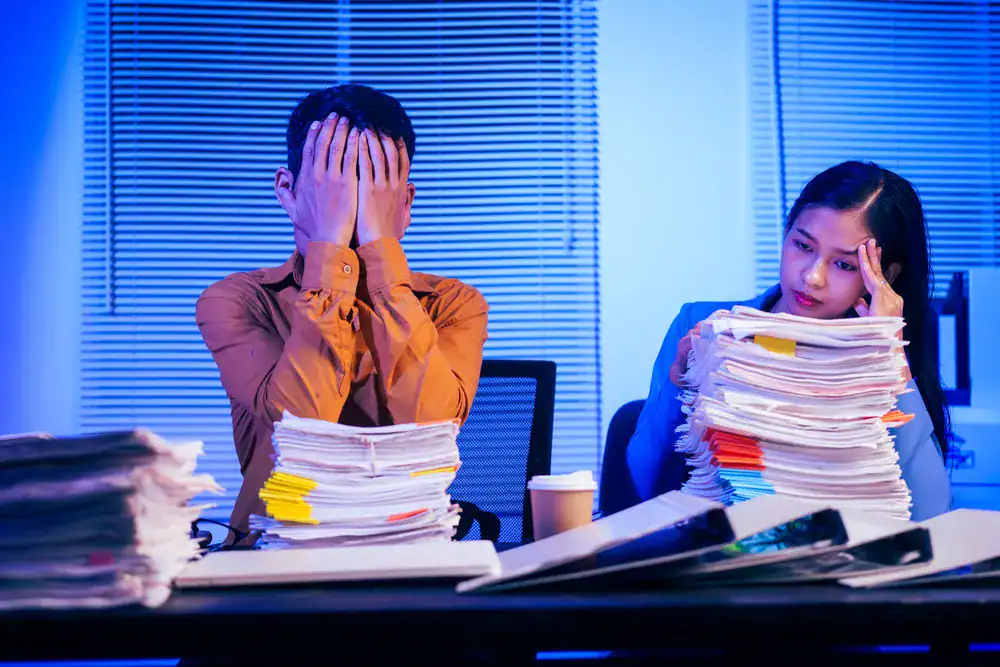 Stressed office workers in Singapore with heavy workload, highlighting heart attack risk and need for a heart specialist in Singapore.