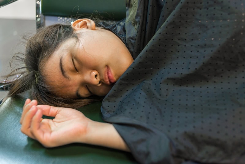 Exhausted woman sleeping in public, showing fatigue as a heart attack warning sign and highlighting when to see a heart specialist in Singapore.