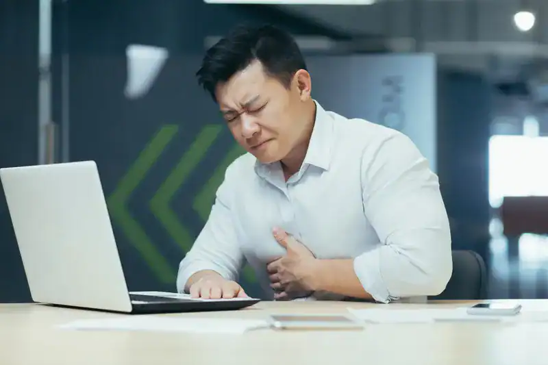 Man experiencing symptoms of blocked arteries while working, a common sign of heart artery blockage.