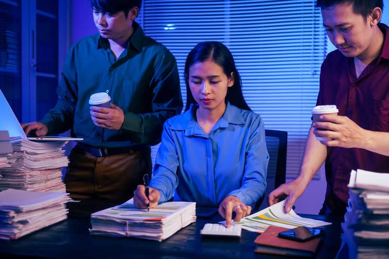 Stressed Singapore office workers doing overtime, showing work pressure linked to heart attack risk and the need for a heart specialist in Singapore.