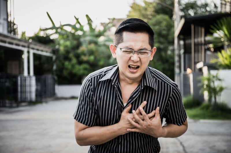 Man clutching his chest in pain, showing possible cardiac arrest symptoms and heart health concerns noted by a heart doctor in Singapore.