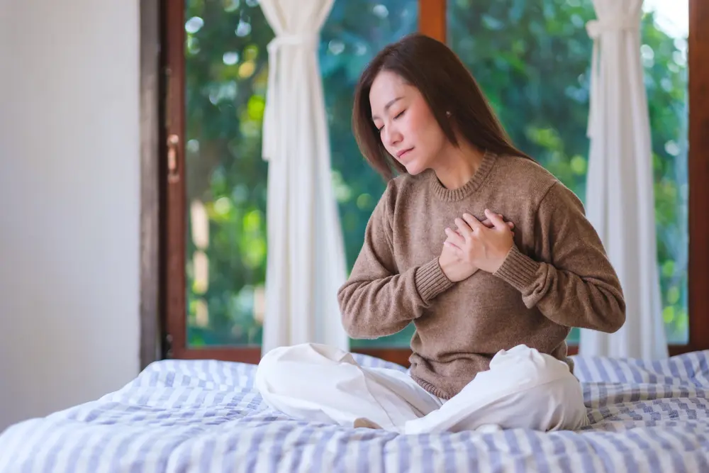 Woman experiencing chest discomfort and palpitations, symptoms that may require Holter monitoring evaluation in Singapore