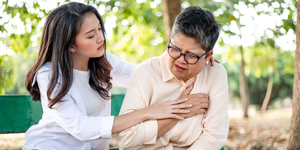 Elderly woman with chest discomfort being assisted, signs of heart disease in women