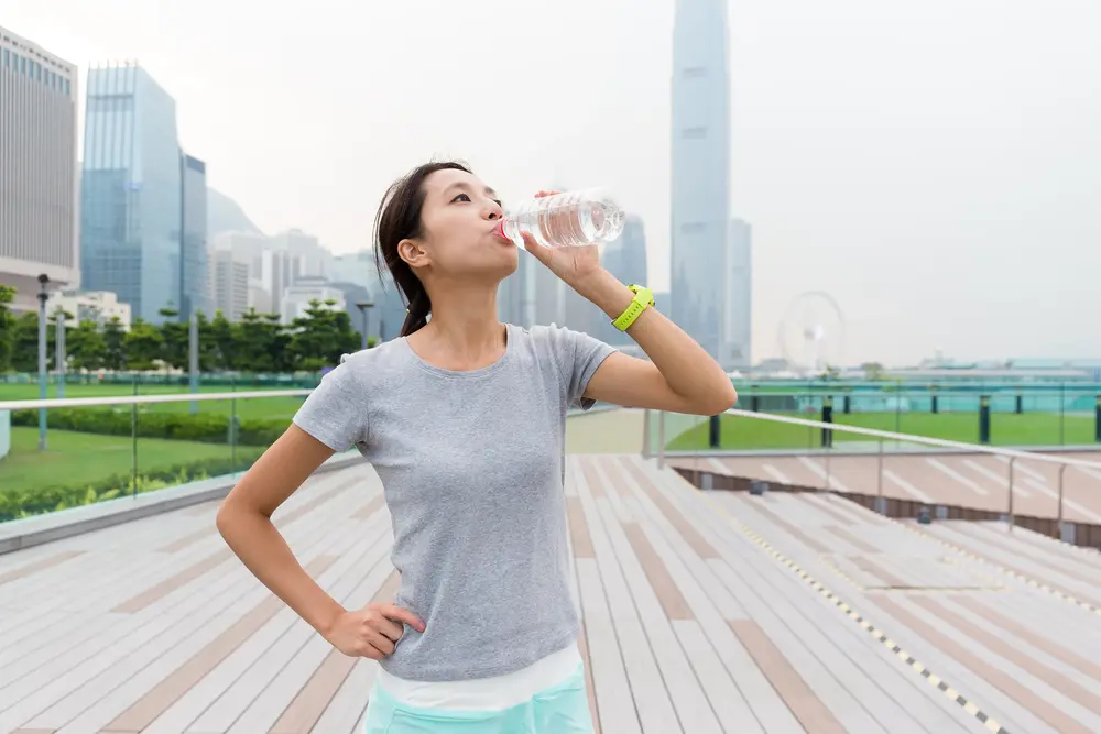 Woman drinking water outdoors to stay hydrated in hot weather and support healthy blood pressure